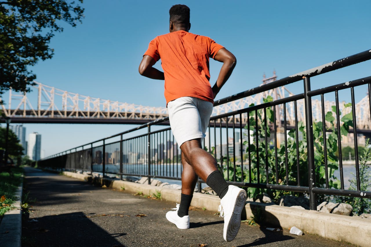 A man jogging on a riverside path, with a city bridge and urban skyline in the background.